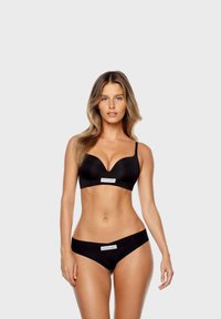 Un set di lingerie nera composto da un reggiseno imbottito con spalline regolabili e un triangolo basso abbinate, entrambi contrassegnati con l'etichetta "GOD SAVE QUEEN".