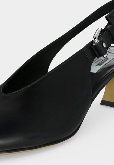 Μαύρο δερμάτινο παπούτσι slingback με ασημένια αγκράφα και χαμηλό χρυσό τακούνι σε λευκό φόντο.