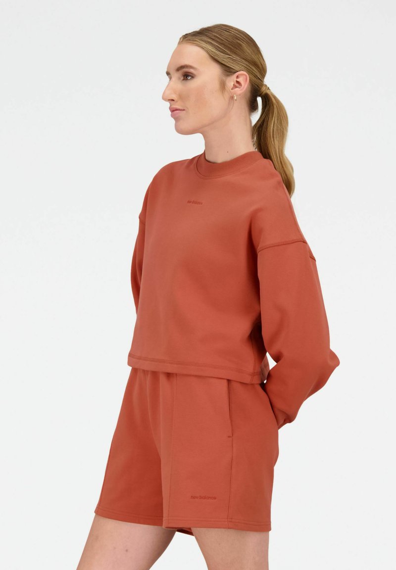Rustkleurige cropped sweatshirt met lange mouwen, zachte textuur en logo-detail op de borst. Gepaarde met bijpassende shorts.