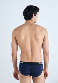 Navyblaue Herrenunterwäsche mit schwarzem elastischem Bund, der das Branding "HUGO" zeigt. Glatte Stoffqualität, enganliegender Schnitt, minimalistisches Design.