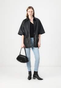 Camisa chaqueta de cuero negro oversized con cuello y cierre de botones, combinada con unos jeans de denim azul claro y botas de tacón negro hasta el tobillo. Llevando un bolso negro.