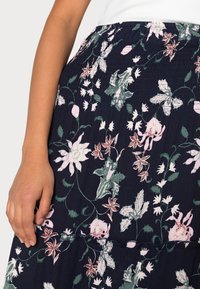 Kwiatowa spódnica midi na granatowym tle, z różowymi i zielonymi motywami roślinnymi, marszczonym pasem i subtelną fakturą.