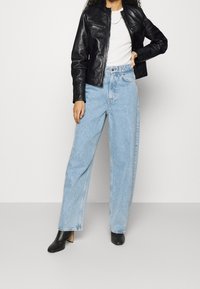 Svart läderjacka med dragkedja fram, kombinerad med ljusblå högmidjade, vida jeans. Svarta höga ankelstövlar.