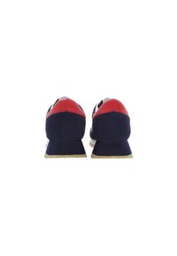 Un paio di sneakers blu navy e rosse viste dal retro, che mostrano il tallone imbottito e le suole beige.
