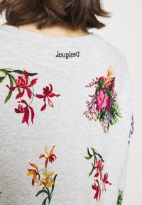 Soft grey sweatshirt with floral print in red, pink, and yellow. Features a round neck and embroidered brand name at the back near the collar.