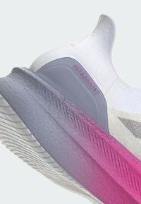 Sneaker bianco con tomaia testurizzata; il tallone grigio presenta la scritta "ULTRABOOST" in rosa. La suola sfumata passa dal grigio al rosa.