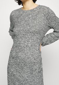 Abito grigio lavorato a maglia con un motivo testurizzato, maniche lunghe, scollatura rotonda e una silhouette comoda con tasche laterali.