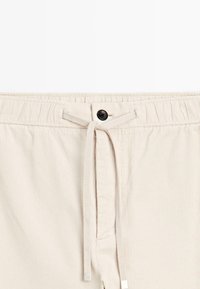 Shorts beige con coulisse caratterizzati da una texture a coste, vita elastica e un bottone nero decorativo sul davanti.
