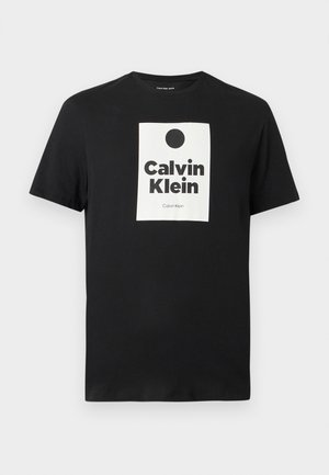 T-shirt noir à manches courtes avec un logo rectangulaire blanc affichant un cercle noir plein au-dessus du texte en gras « Calvin Klein ».