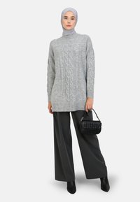 Lys grå kabelstrik sweater med høj krave, parret med mørk grå brede bukser, en sort tekstureret håndtaske og sorte hælede støvler.