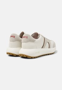 Bílé kožené tenisky s hladkým povrchem, zaobleným tvarem a hnědými detaily. Červené logo „CAMper“ na patě a strukturovaná podešev.