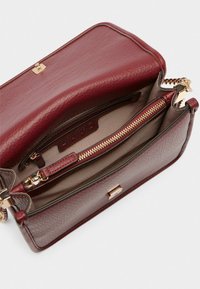 Bordeaux læder håndtaske med guldfarvet hardware, der har et lynlåslommer, glat inderfor og en struktureret design.