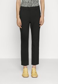 Černé kalhoty na míru s úzkým střihem a zkrácenou délkou, doplněné žlutými mokasínami. Hladká látka a minimální detaily.