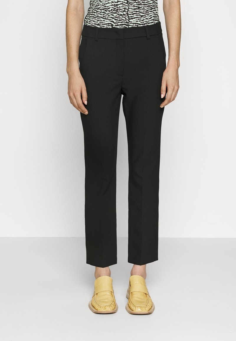 Černé kalhoty na míru s úzkým střihem a zkrácenou délkou, doplněné žlutými mokasínami. Hladká látka a minimální detaily.