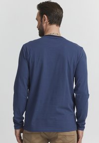 Hosszú ujjú tengerészkék pamut ing, kerek nyakkivágással és sima felülettel, hátul enyhe varrással. Relaxált illeszkedésre tervezve.
