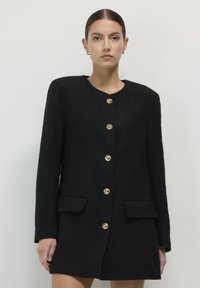 Blazer nero con texture, scollo rotondo, bottoni dorati lungo la parte anteriore e due tasche frontali, progettato per una vestibilità sartoriale.