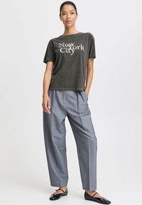 Cotton dark gray T-shirt with "New York City" text. Loose fit, paired with light gray pleated trousers and black flats.