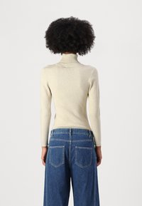 Kremfarget ribbestrikket turtleneck genser, lange ermer, tettsittende design, kombinert med høy midje blå vide jeans med baklommer og denimtekstur.