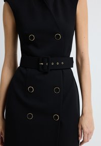 Czarna sukienka z podwójnym zapięciem, ozdobiona okrągłymi guzikami w kolorze złotym oraz pasującym paskiem z tkaniny z kwadratową klamrą i detalami w postaci oczek.