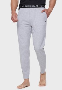 Graue Baumwoll-Jogginghosen mit einem schwarzen Elastikbund, auf dem der Text "THREADBARE" steht. Bündchen an den Knöcheln; minimalistisches Design.