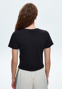 T-shirt nera a maniche corte con scollatura a girocollo, realizzata in tessuto morbido, con orlo cropped e superficie liscia.