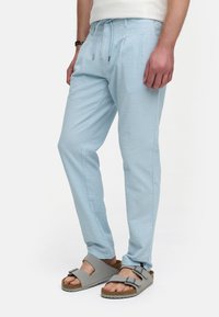 Helle blaue, strukturierte Hose mit verstellbarem Bund, mit vorderen Falten und Seitentaschen, kombiniert mit grauen Sandalen.