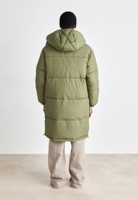 Olive green puffer coat with a hood, quilted design, long sleeves, and a longer length. Features elastic cuffs and side slits.