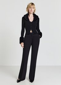 Schwarze gerippte Strickjacke mit einem Kragen und Besätzen aus Kunstfell, kombiniert mit schwarzen weit geschnittenen Hosen und schwarzen spitzen Absätzen.