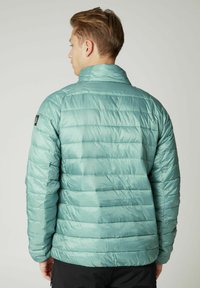 Lagani, pufasti tirkizni kaput s horizontalnim kvadratnim dizajnom, visokim ovratnikom i logotipom na lijevom ramenu. Glatka, sjajna tkanina.