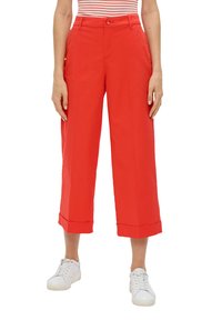 Czerwone szerokie spodnie 7/8 z podwiniętymi nogawkami, wykonane z lekkiego materiału. W połączeniu z białymi sneakersami dla uzyskania swobodnego wyglądu.