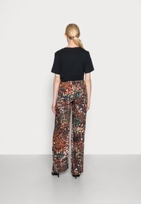 Zwarte t-shirt gecombineerd met wijde, gebloemde broek met multikleurige abstracte ontwerpen in oranje, groen en metallic accenten.