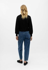 Felpa nera con maniche oversize, abbinata a jeans blu a vita alta con due tasche posteriori e vestibilità dritta.