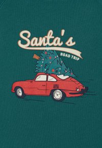 Czerwony, klasyczny samochód z choinką na dachu, na tle ciemnozielonym, z zabawnym napisem: "Droga Świętego Mikołaja."