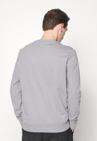 Sudadera gris hecha de una tela suave, con mangas largas, cuello redondo y puños y dobladillo acanalados. Sin patrones ni logotipos visibles.