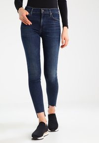 Smala jeans i mörkblå denim med hög midja, subtila blekningar och rå kant. Tillsammans med svarta slip-on skor.