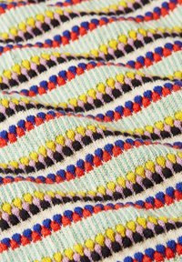 Strickstoff mit einem welligen Muster aus bunten Kugeln in Gelb, Rot, Lila, Blau und Schwarz auf einem hellen Mint-Hintergrund.
