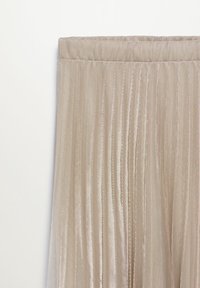 Jupe plissée beige avec une ceinture élastique en tissu léger et brillant sur un fond clair uni.