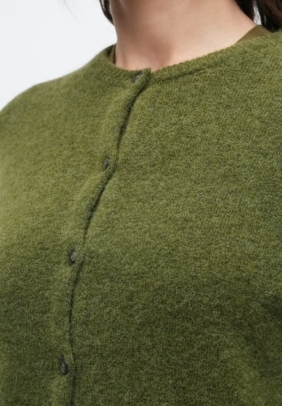 Πράσινη μάλλινη ζακέτα με στρογγυλεμένο λαιμόκοψη, κούμπωμα με κουμπιά και μαλακή, υφασμάτινη υφή. Το ύφασμα έχει ελαφρώς χνουδωτή εμφάνιση.