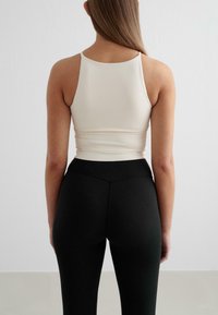 Top aderente bianco a spalline sottili, abbinato a leggings neri a vita alta. Tessuto liscio, design minimalista.