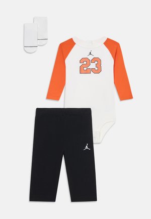 Ensemble de vêtements pour bébé comprenant un body blanc avec des manches raglan orange et un graphique "23", associé à un legging noir et des chaussettes blanches.