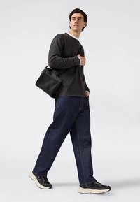 Schwarzes Langarmshirt, dunkelblaue Jeans in lockerer Passform, schwarze Umhängetasche und schwarze Turnschuhe mit cremefarbenen Sohlen. Lässiges Outfit mit schlichtem Design.