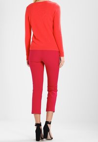 Rode trui met een ronde hals, slim fit en geribde manchetten, gecombineerd met aansluitende roze broeken die tot boven de enkel zijn geknipt, gedragen met zwarte hoge hakken.