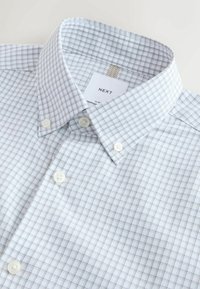 Valkoinen ruudullinen nappipaita kapealla kauluksella. Kankaassa on pieni ruutukuvio vaaleanharmaana ja sinisenä, ja paidassa on valkoiset napit.