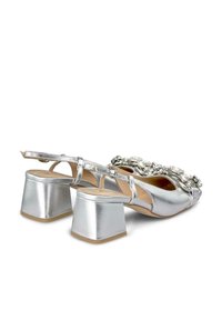 Sandali argentati con tacco a blocco chunky, arricchiti da dettagli decorativi sul davanti e una cintura alla caviglia sicura.