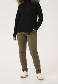 Svart zip-up tröja med en strukturerad yta, kombinerad med olivgröna byxor och vita sneakers med en beige sula. Avslappnad outfit.