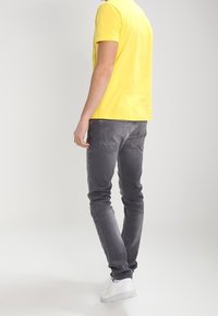 Žluté tričko s krátkým rukávem, šedé slim-fit džíny se zadními kapsami a bílé tenisky. Zaměření na ležérní, moderní design a střih.