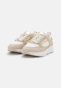 Beige and white sneakers with metallic gold accents, textured overlays, and white laces. Thick sole with a slight elevation for added comfort.