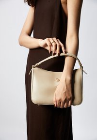 Sac à main en cuir beige au design épuré, avec une anse supérieure et des accents en métal doré. Texture lisse, forme légèrement arrondie.
