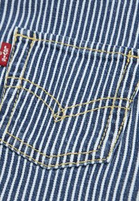 Tissu en denim rayé bleu et blanc avec une petite poche à couture jaune. Comprend une étiquette rouge sur le côté.