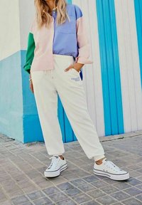 Chemise à boutons multicolore (rose pastel, bleu, vert) associée à un pantalon de jogging blanc et des baskets blanches classiques à rayures noires.